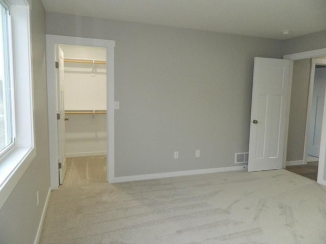 unfurnished bedroom featuring a closet, a spacious closet, and light carpet