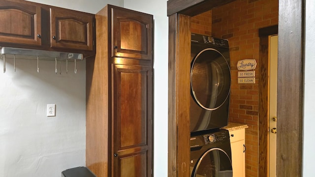 clothes washing area with cabinets, stacked washer / dryer, and brick wall