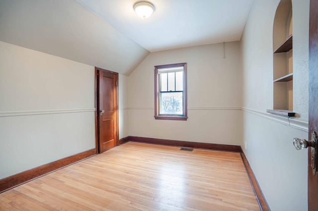 additional living space with built in features, vaulted ceiling, and light hardwood / wood-style flooring