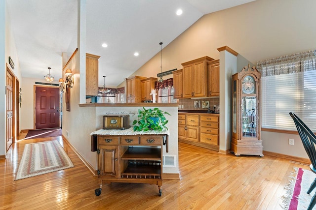 kitchen with kitchen peninsula, decorative light fixtures, light hardwood / wood-style floors, tasteful backsplash, and high vaulted ceiling