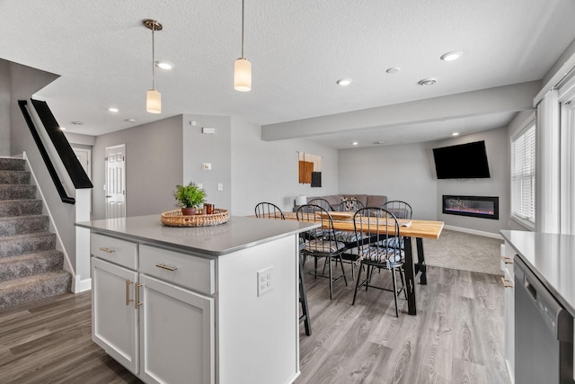 kitchen with pendant lighting, black dishwasher, light hardwood / wood-style floors, white cabinets, and a kitchen island