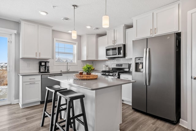 kitchen with appliances with stainless steel finishes, pendant lighting, white cabinetry, sink, and a center island