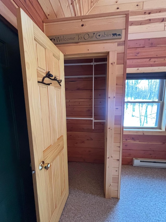 interior space with carpet, a baseboard heating unit, and wood walls