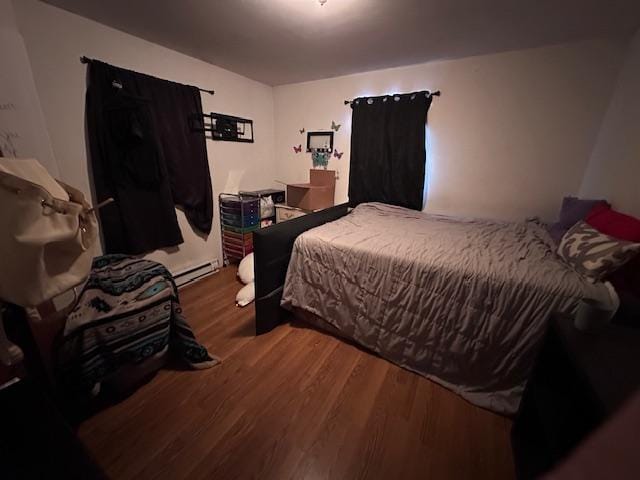 bedroom with dark hardwood / wood-style floors and a baseboard heating unit