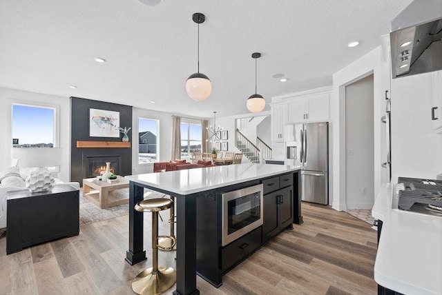 kitchen with a center island, hanging light fixtures, built in microwave, stainless steel refrigerator with ice dispenser, and white cabinets