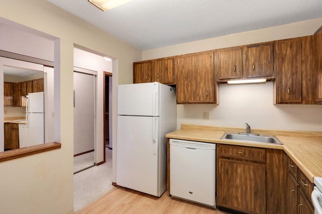 kitchen featuring white appliances, light hardwood / wood-style floors, a textured ceiling, and sink