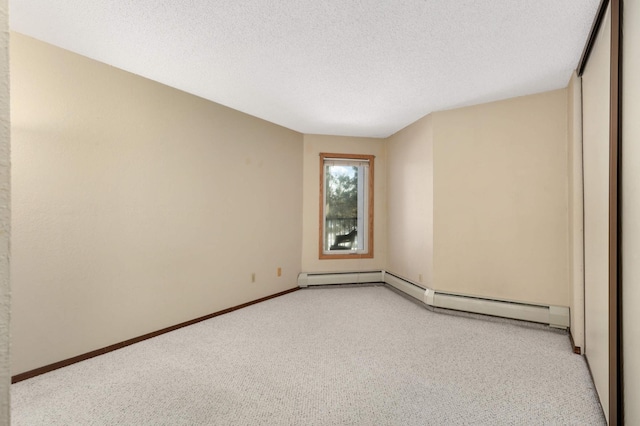 spare room with a textured ceiling, light colored carpet, and a baseboard heating unit