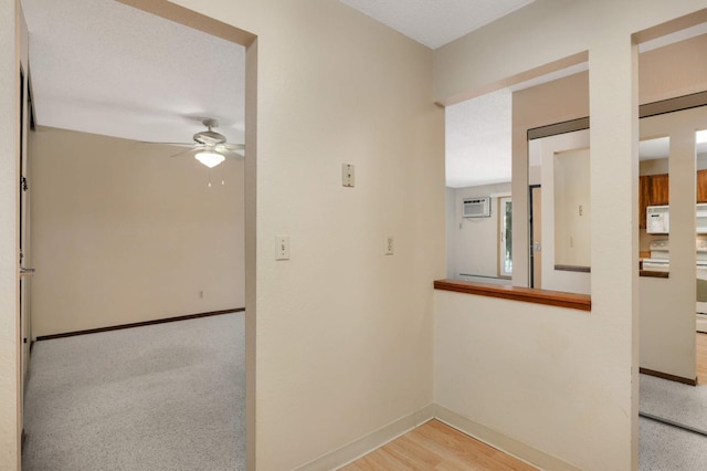 hall with light wood-type flooring, a wall mounted air conditioner, and a textured ceiling