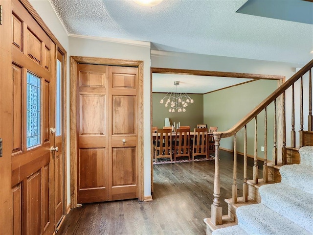 foyer entrance featuring a notable chandelier, dark hardwood / wood-style flooring, a textured ceiling, and ornamental molding