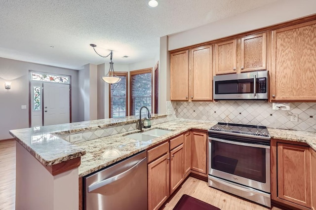 kitchen featuring kitchen peninsula, tasteful backsplash, stainless steel appliances, sink, and hanging light fixtures