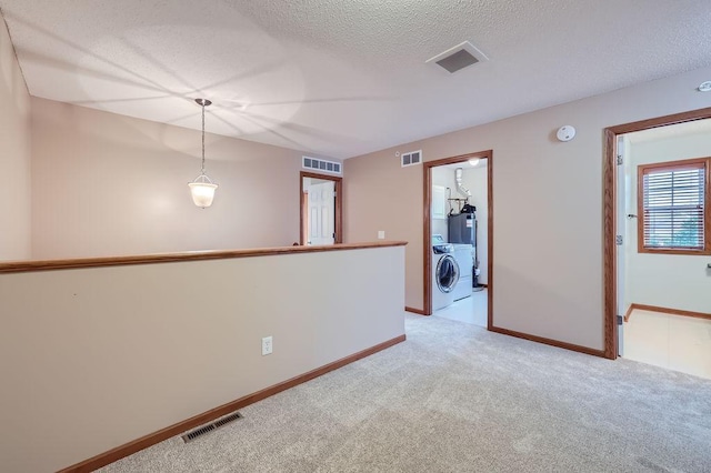 empty room with light colored carpet, a textured ceiling, and independent washer and dryer