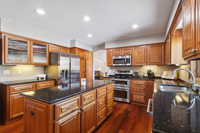 kitchen with sink, appliances with stainless steel finishes, dark stone countertops, a center island, and dark hardwood / wood-style flooring