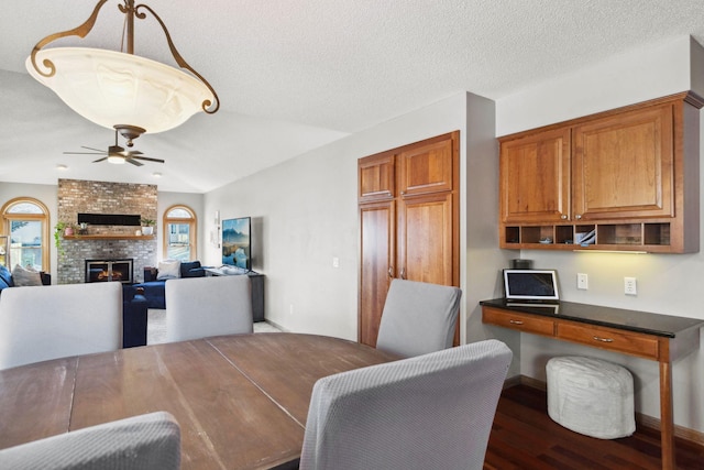 dining room featuring dark wood-type flooring, ceiling fan, a fireplace, and a textured ceiling