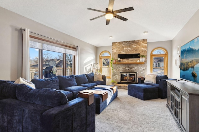 living room featuring ceiling fan, a textured ceiling, a brick fireplace, vaulted ceiling, and light colored carpet