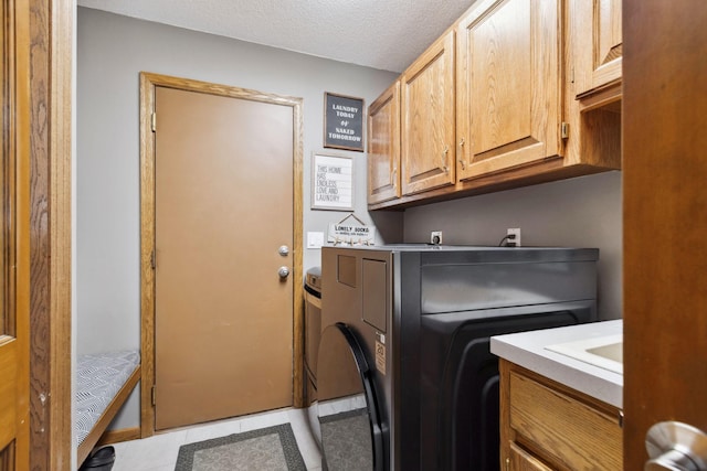 clothes washing area featuring cabinets, washer / clothes dryer, a textured ceiling, and light tile patterned floors