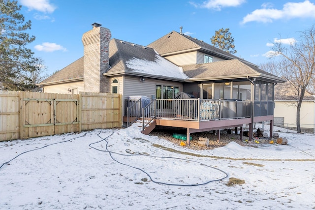 snow covered back of property featuring a deck with water view and a sunroom