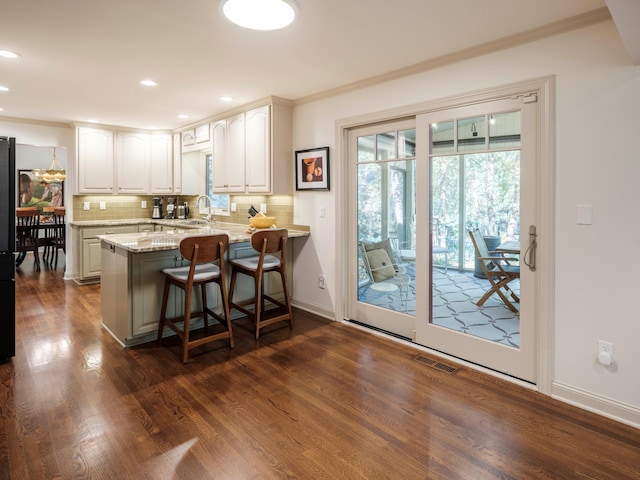 kitchen featuring kitchen peninsula, decorative backsplash, dark hardwood / wood-style flooring, white cabinets, and a kitchen breakfast bar