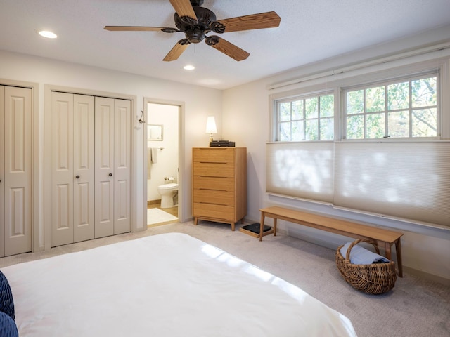 bedroom with ensuite bathroom, light colored carpet, ceiling fan, and multiple closets