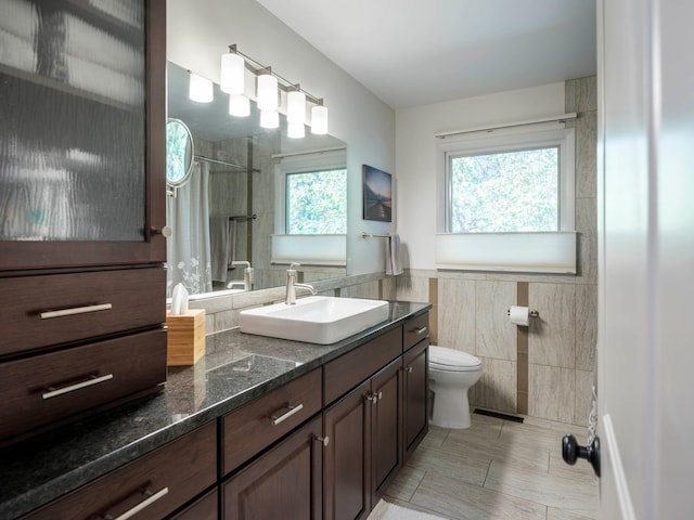 bathroom featuring a tile shower, toilet, vanity, and tile walls