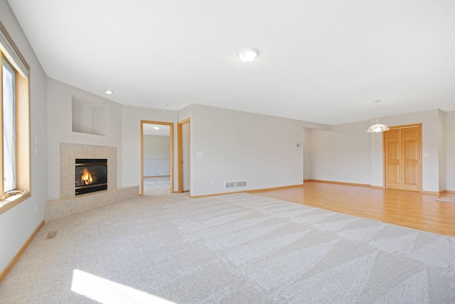 unfurnished living room featuring light carpet and a tiled fireplace