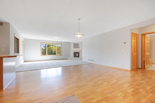 unfurnished living room with a textured ceiling, an inviting chandelier, and light hardwood / wood-style flooring