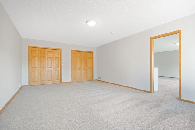 unfurnished bedroom featuring two closets and light colored carpet