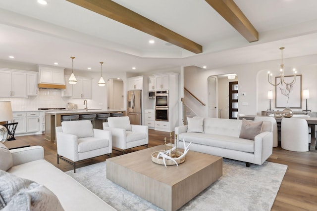 living room featuring an inviting chandelier, beam ceiling, light hardwood / wood-style floors, and sink