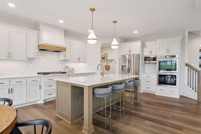 kitchen featuring a center island with sink, stainless steel appliances, dark hardwood / wood-style flooring, pendant lighting, and white cabinets