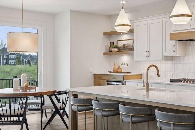 kitchen with sink, white cabinetry, pendant lighting, decorative backsplash, and a breakfast bar