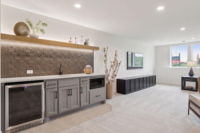 bar featuring beverage cooler, light colored carpet, gray cabinetry, black microwave, and sink