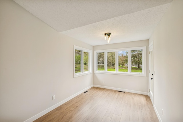 unfurnished room with a textured ceiling, baseboards, visible vents, and light wood finished floors