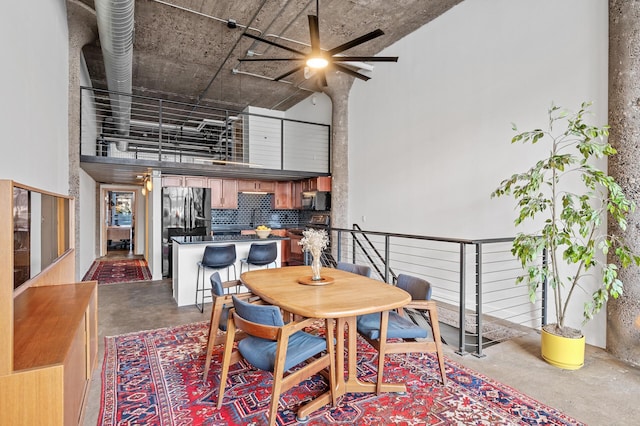 dining space featuring concrete flooring, ceiling fan, and a high ceiling