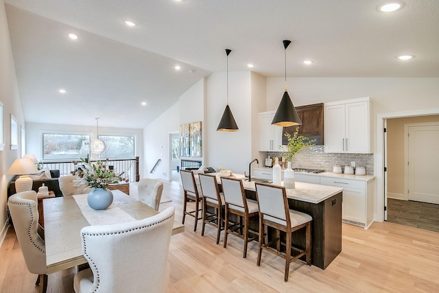 kitchen featuring decorative backsplash, a kitchen island with sink, pendant lighting, light hardwood / wood-style flooring, and white cabinetry