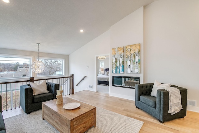 living room featuring high vaulted ceiling, hardwood / wood-style flooring, and an inviting chandelier