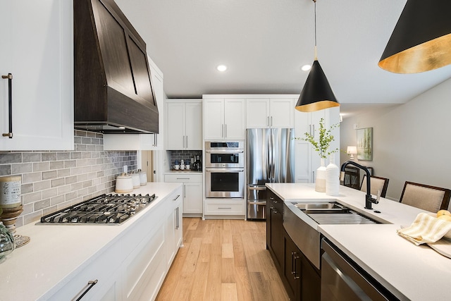 kitchen with tasteful backsplash, custom exhaust hood, stainless steel appliances, sink, and pendant lighting