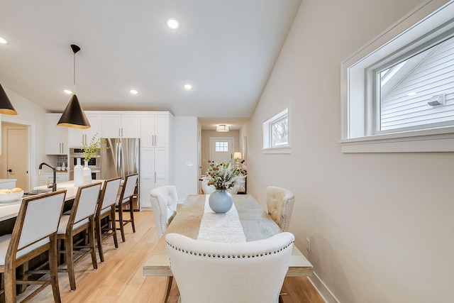 dining room featuring sink, light hardwood / wood-style floors, and vaulted ceiling