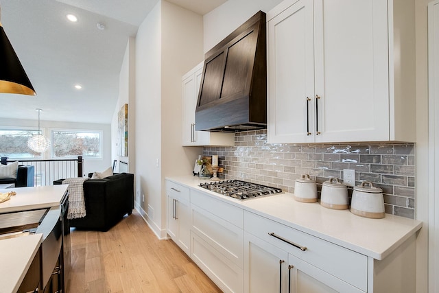 kitchen with decorative backsplash, premium range hood, stainless steel gas cooktop, pendant lighting, and white cabinets