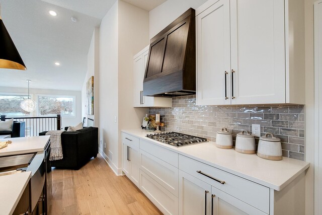 kitchen with backsplash, pendant lighting, stainless steel gas stovetop, white cabinets, and custom exhaust hood