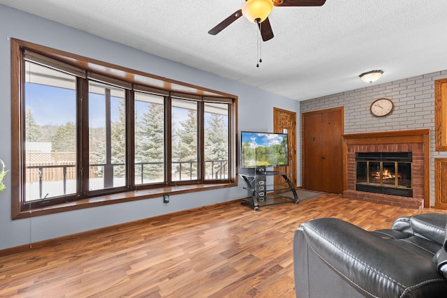 living room featuring ceiling fan, a fireplace, a textured ceiling, and light wood-type flooring