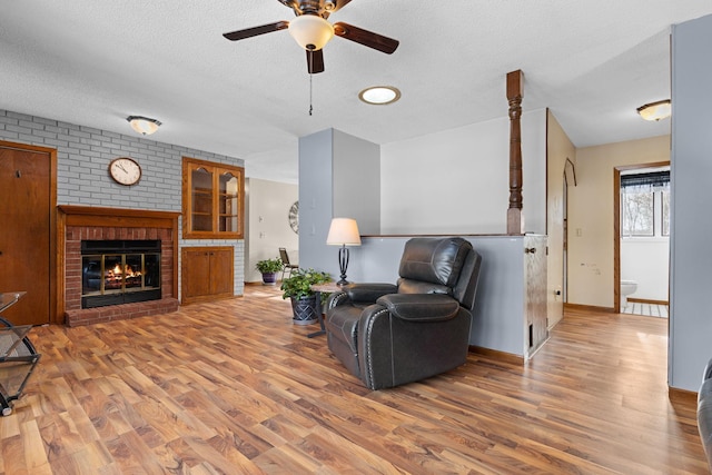 living room featuring ceiling fan, wood-type flooring, a brick fireplace, and a textured ceiling