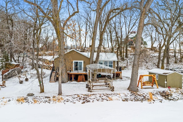 snow covered rear of property featuring a deck and a storage shed