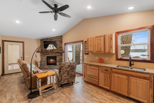 kitchen with ceiling fan, a fireplace, light stone countertops, vaulted ceiling, and sink