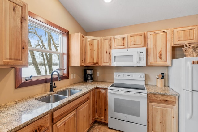 kitchen featuring light brown cabinets, white appliances, vaulted ceiling, light stone counters, and sink