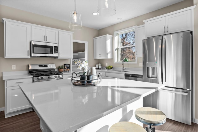 kitchen with pendant lighting, sink, stainless steel appliances, white cabinets, and a kitchen island