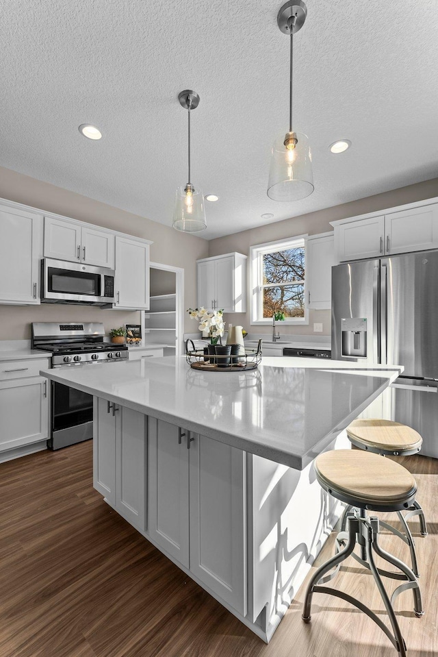 kitchen featuring decorative light fixtures, a kitchen island, white cabinets, and appliances with stainless steel finishes