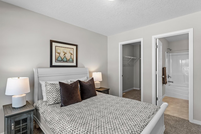 carpeted bedroom featuring a walk in closet, a closet, a textured ceiling, and ensuite bathroom