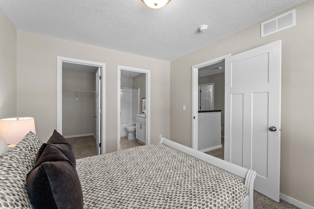 bedroom with connected bathroom, a spacious closet, a textured ceiling, carpet flooring, and a closet