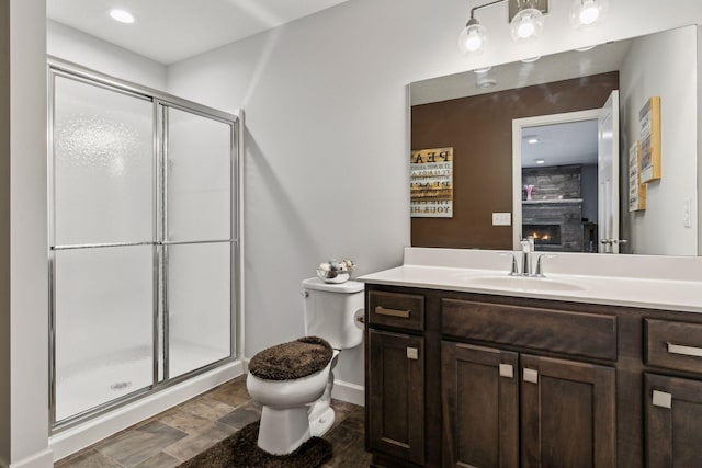 bathroom featuring toilet, vanity, a fireplace, and a shower with door