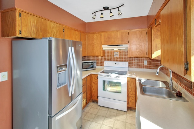 kitchen featuring under cabinet range hood, stainless steel appliances, a sink, light countertops, and brown cabinetry