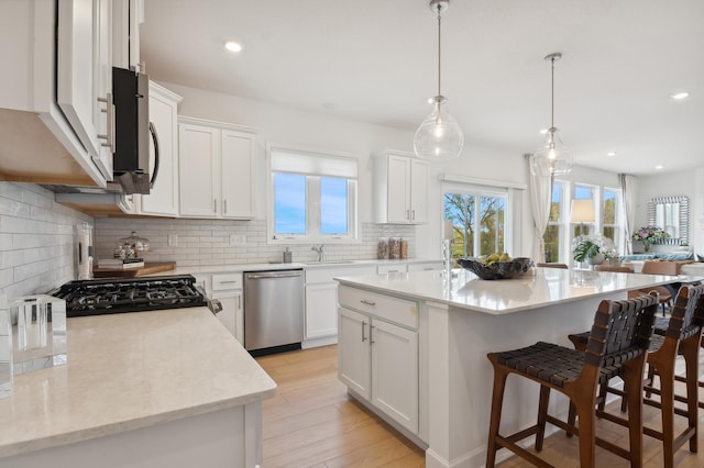 kitchen featuring backsplash, stainless steel dishwasher, a center island with sink, white cabinets, and hanging light fixtures